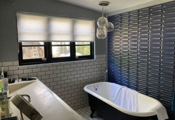 Bathroom window in San Marcos with custom sheer window shades half open, allowing sunlight while maintaining a cozy atmosphere.