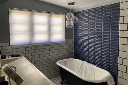 Elegant bathroom showcasing high quality custom pull down window shades and unique blue wall tiles behind a freestanding tub.